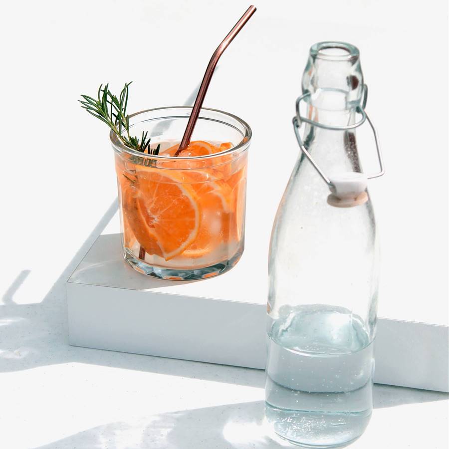 Vaso de agua con rodajas de naranja y rama de romero