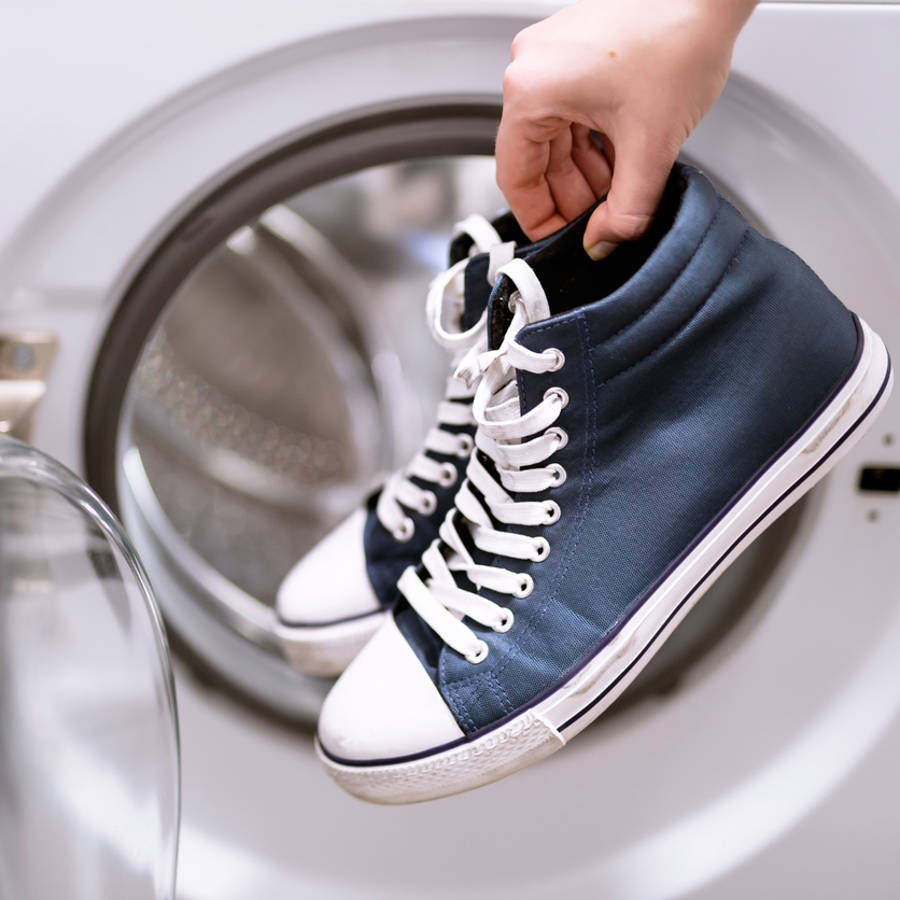 Mujer sosteniendo unas zapatillas junto a una lavadora
