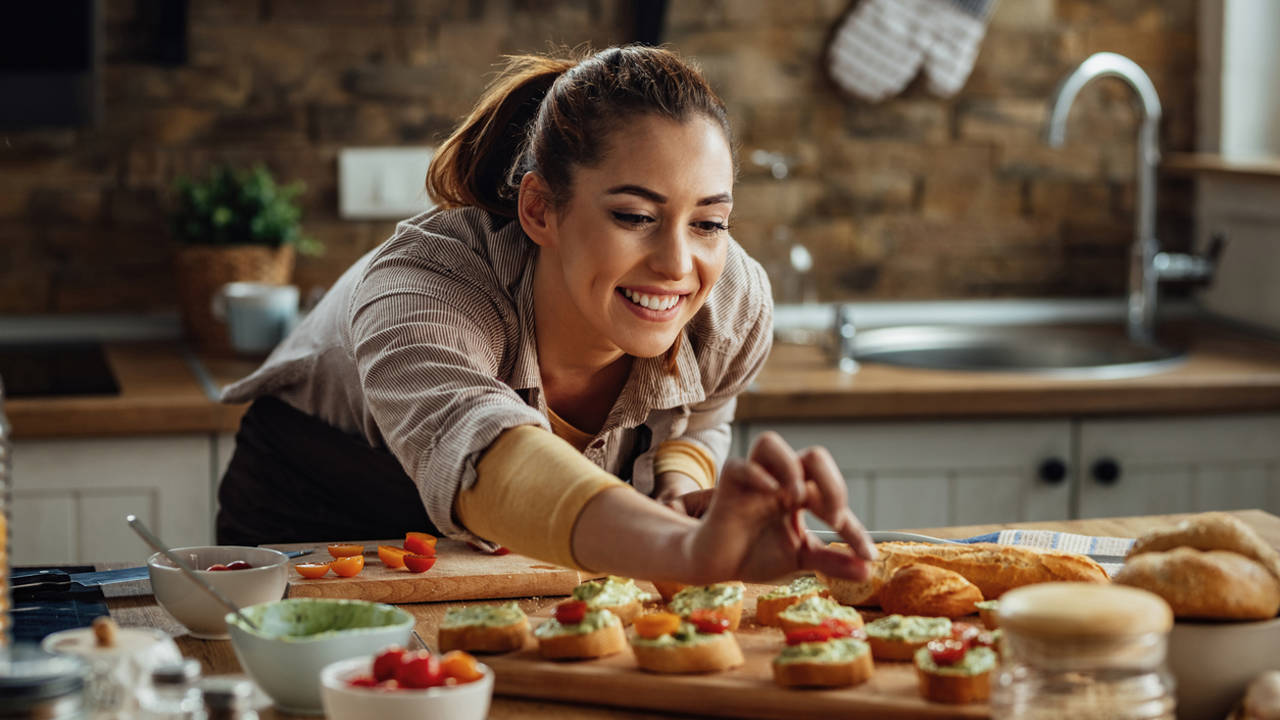 Mujer joven en la cocina preparando canapés bocadillos montaditos