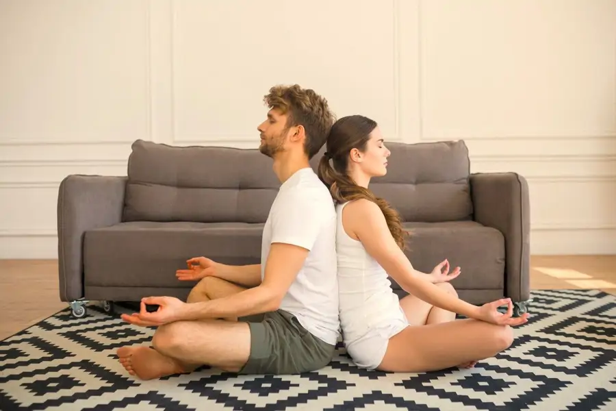 Pareja meditando en el salón apoyados el uno en el otro