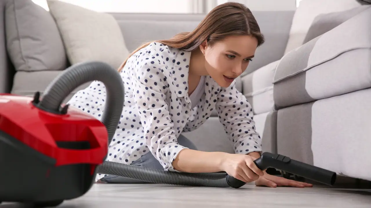mujer limpiando debajo del sofá